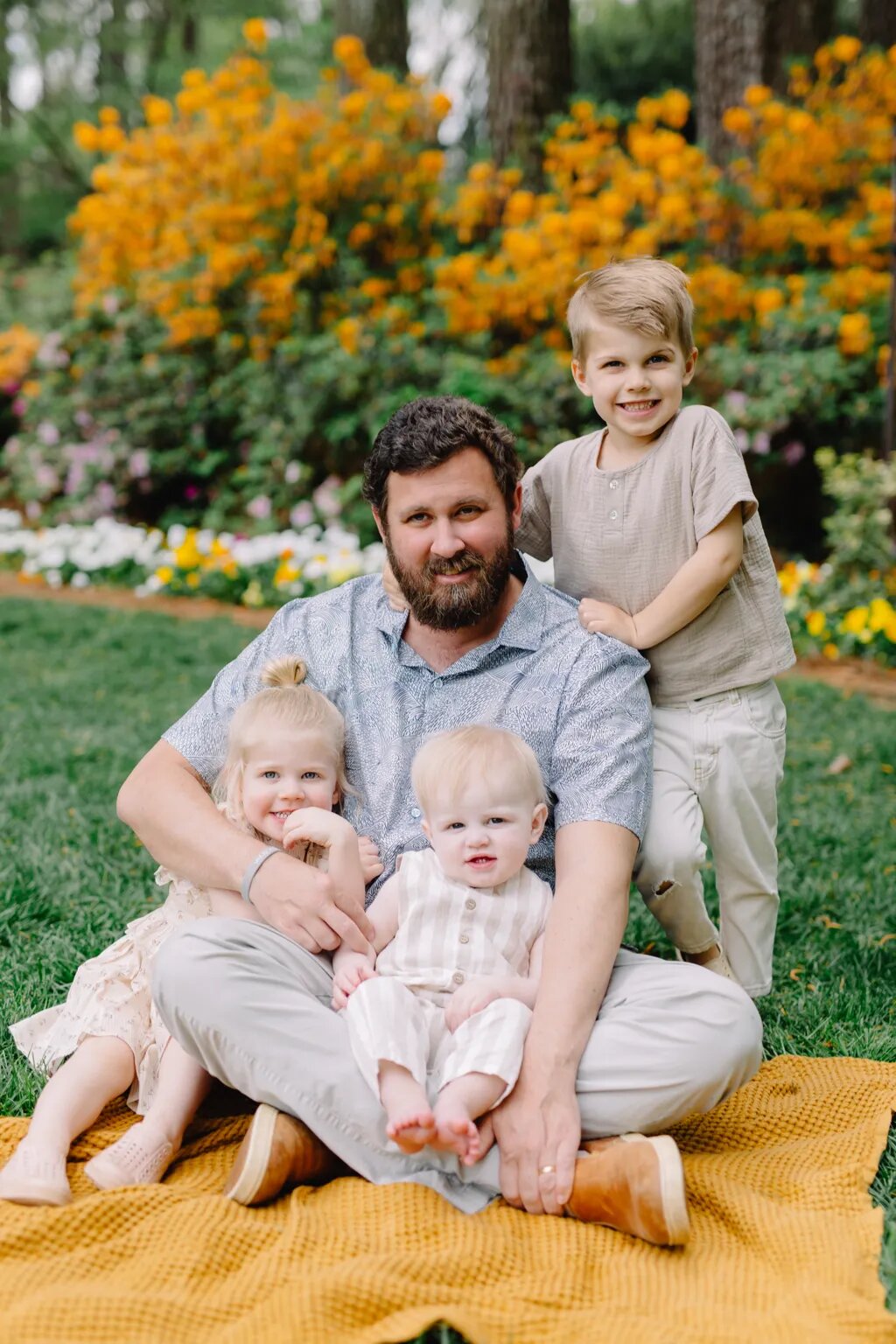 Bryan sitting on a blanket with Huck, Elliot and Foster among flowers