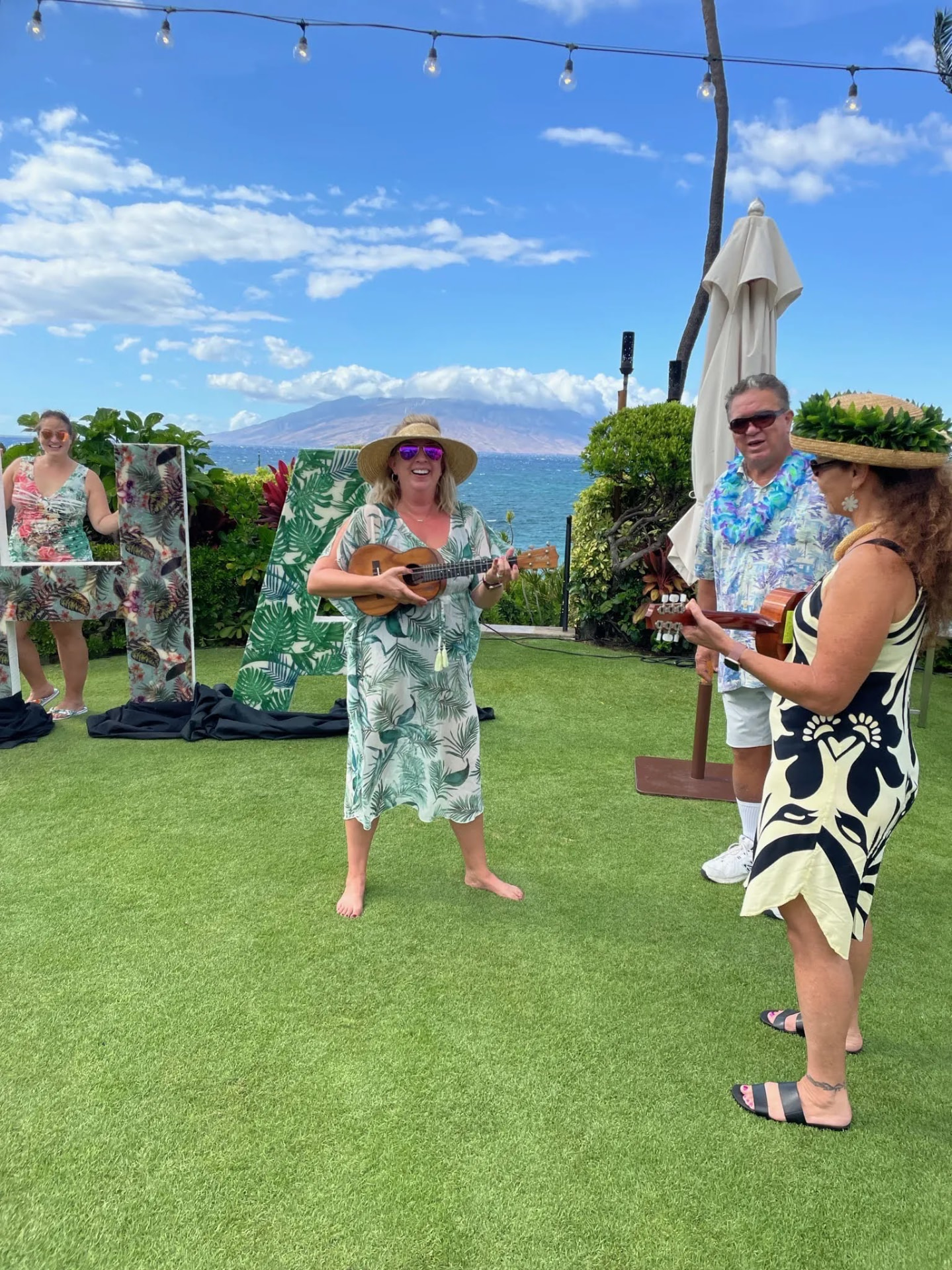 Emily in a sun hat playing ukulele on a lawn by the ocean in Hawaii